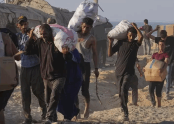 Des Palestiniens transportant des sacs et cartons d'aide humanitaire destinés à l'enclave de Gaza (Crédit : AP)