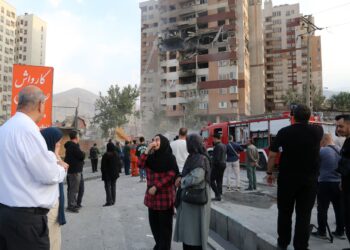 Des secouristes iraniens et des habitants rassemblés devant un immeuble endommagé à Téhéran, au lendemain des frappes israéliennes.