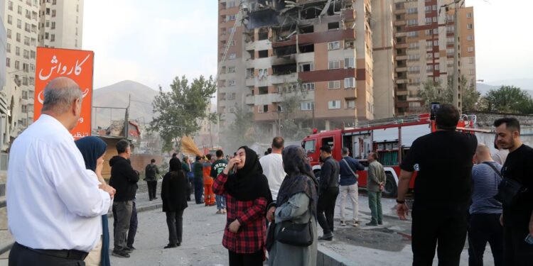 Des secouristes iraniens et des habitants rassemblés devant un immeuble endommagé à Téhéran, au lendemain des frappes israéliennes.